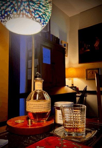 Bottle of Blantons bourbon with a glass of whiskey under a colorful lamp